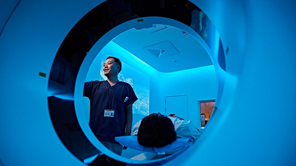 Imagem do médico a configurar um exame na gantry do aparelho de TC, com o paciente na mesa do paciente do sistema de TC