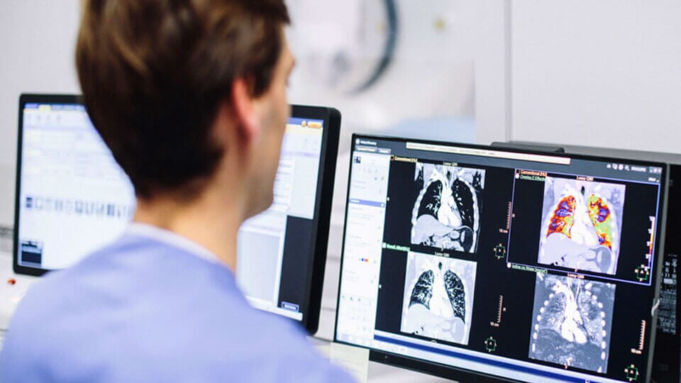 Imagem do técnico a analisar imagens clínicas de TC num monitor