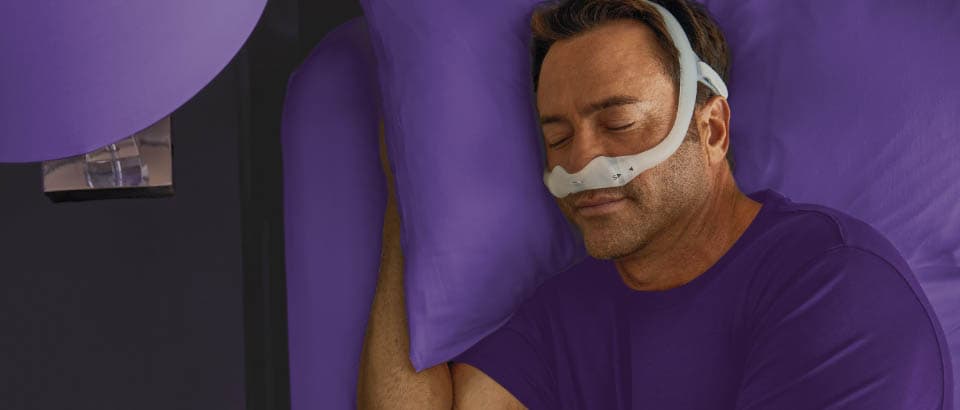 Homem dormindo de máscara e usando uma camiseta roxa