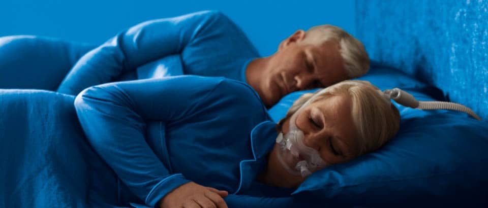 Mulheres vestidas de azul dormindo de lado e usando uma máscara e um homem vestido de azul dormindo de lado
