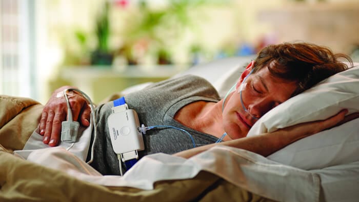 Fotografia de um homem na cama, dormindo de lado, utilizando equipamento de teste de sono da Philips
