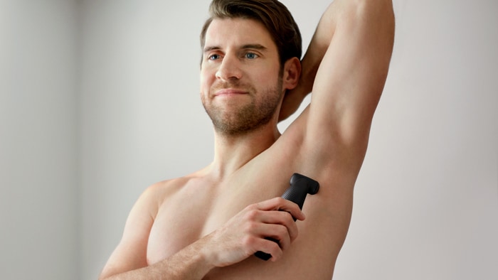 O torso bem barbeado de um homem usando uma máquina de barbear Philips Bodygroom para depilar as axilas