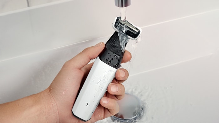 Uma mão segurando um aparador corporal Philips sob uma torneira, enxaguando-o com água.